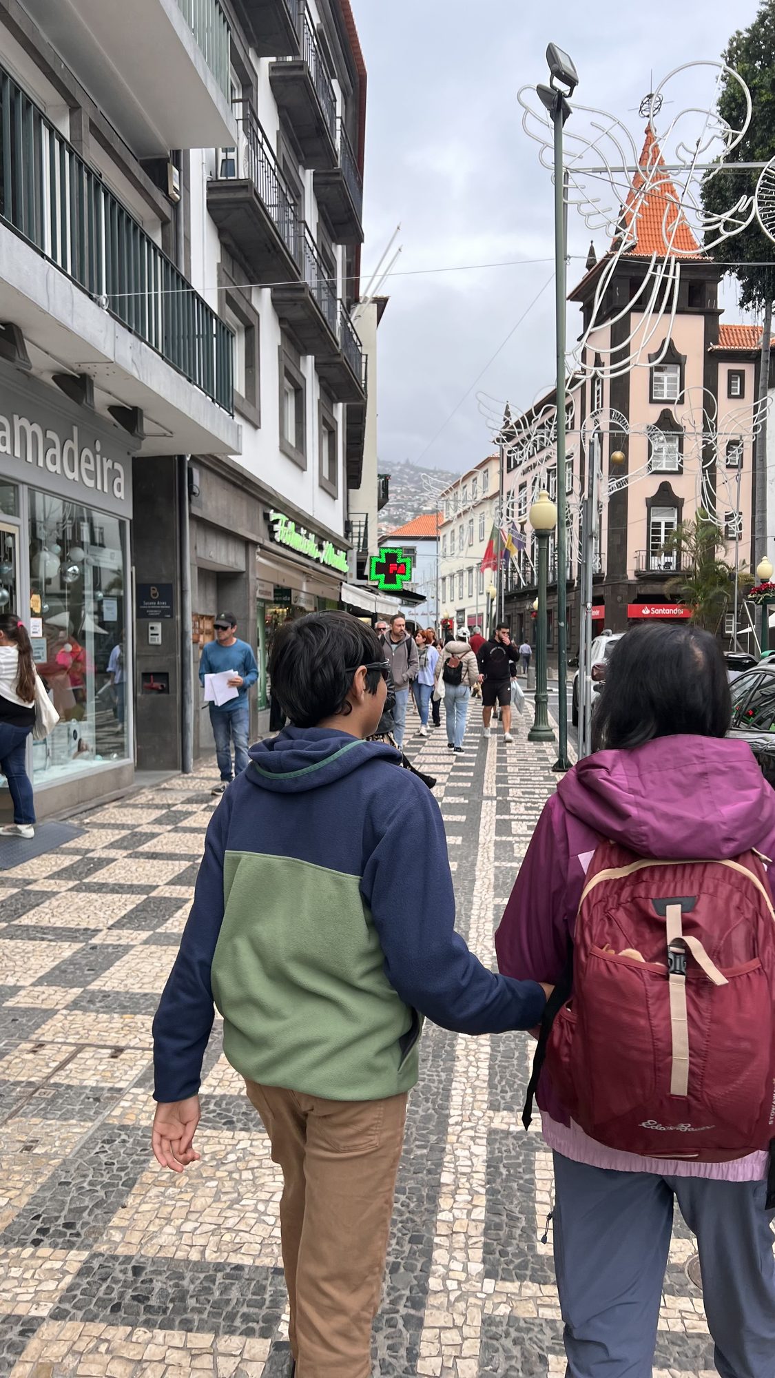 Two of us walking arm in arm along a busy shopping street with black and white patterned pavement.