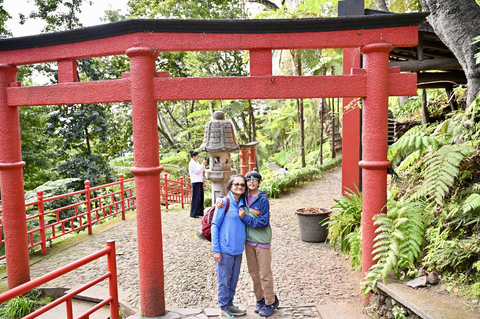 Two of us standing under a red Japanese gate, beside red railings and a stone lantern.