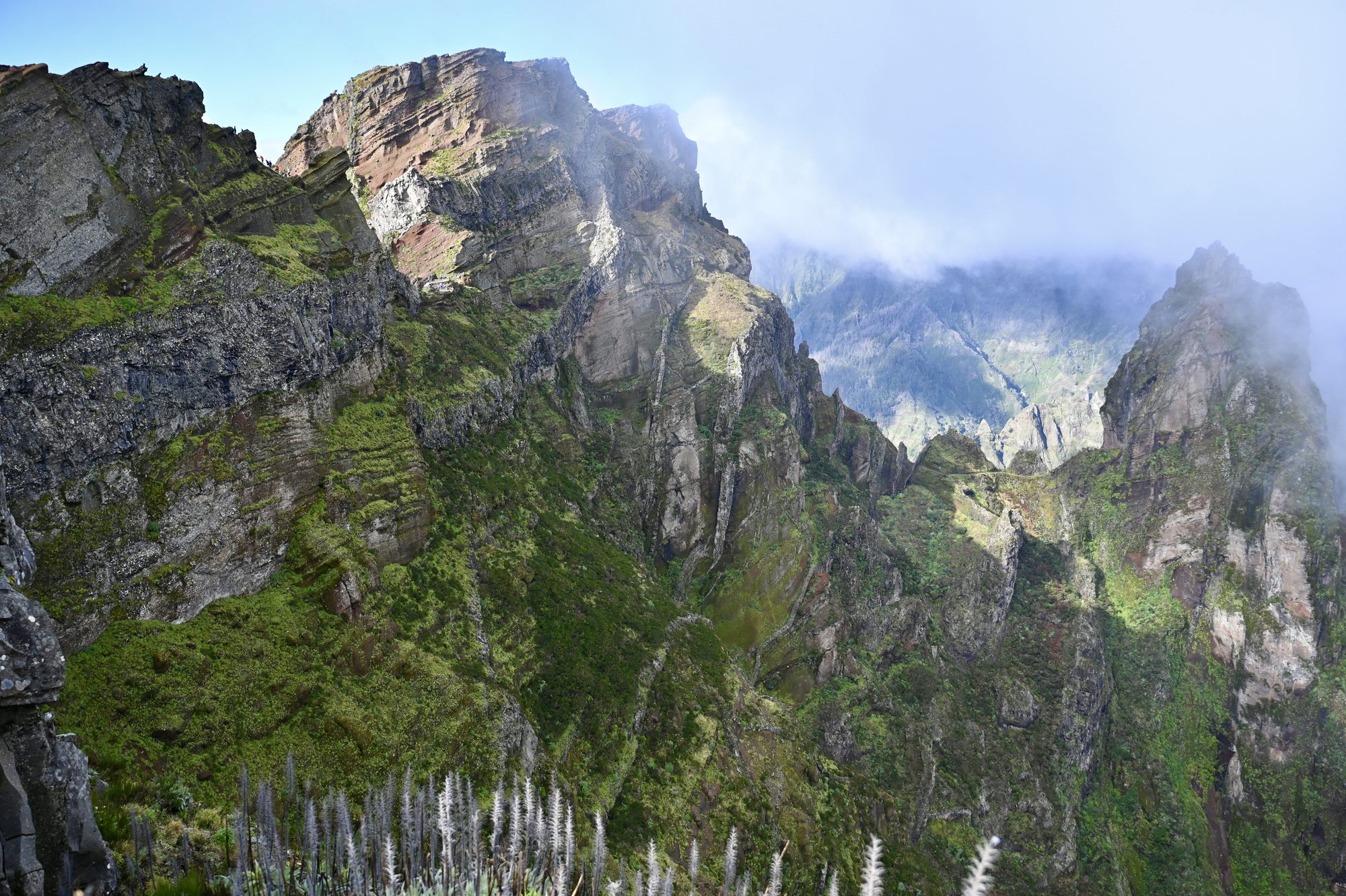 Sheer green and rust-coloured cliffs and pinnacles, with fog drifting through the valleys behind.
