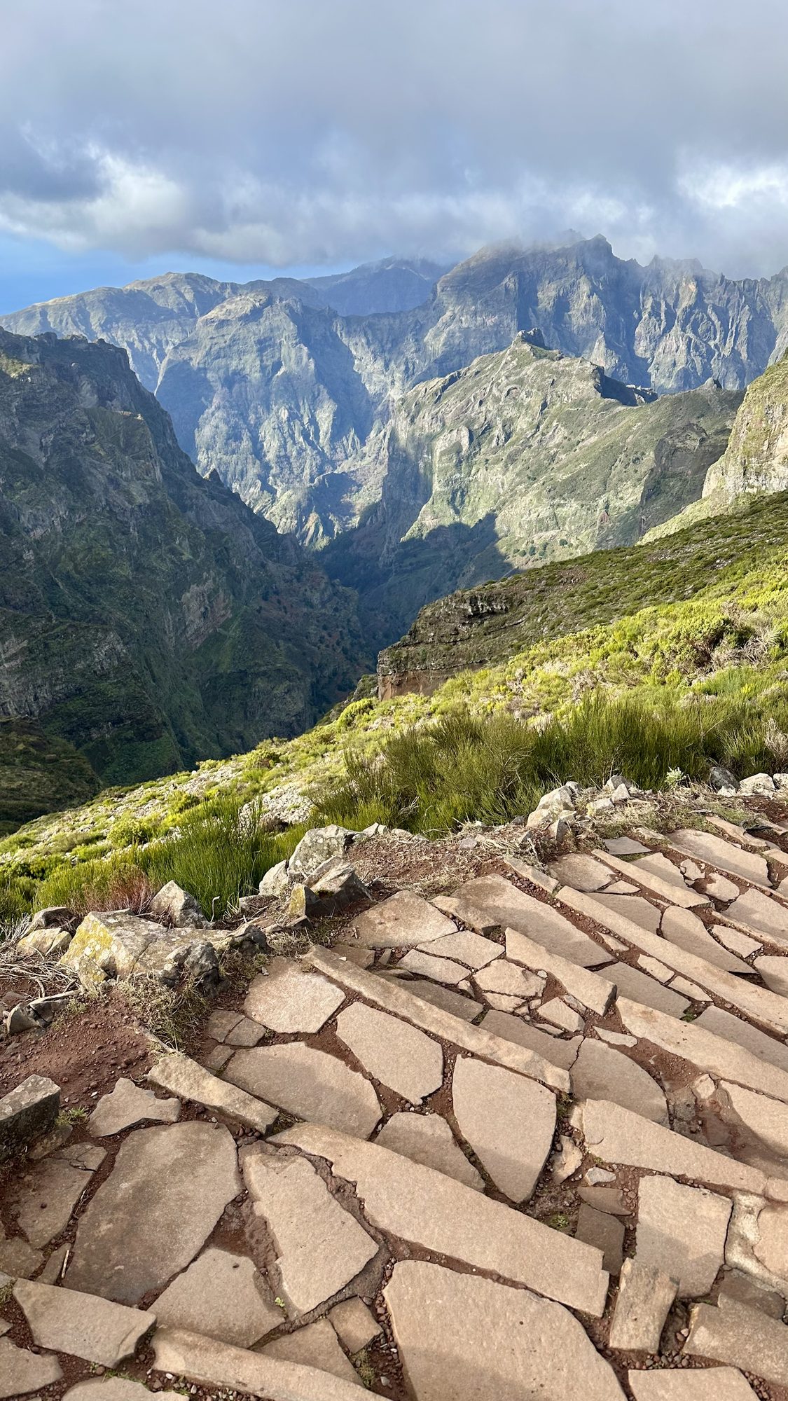 Worn stone steps in the foreground, with jagged green mountains and clouds lifting off the peaks beyond.