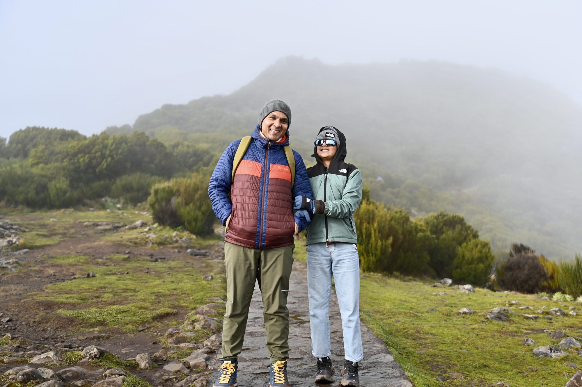 Two of us in warm jackets standing on the stone trail, with the hillside behind disappearing into thick fog.