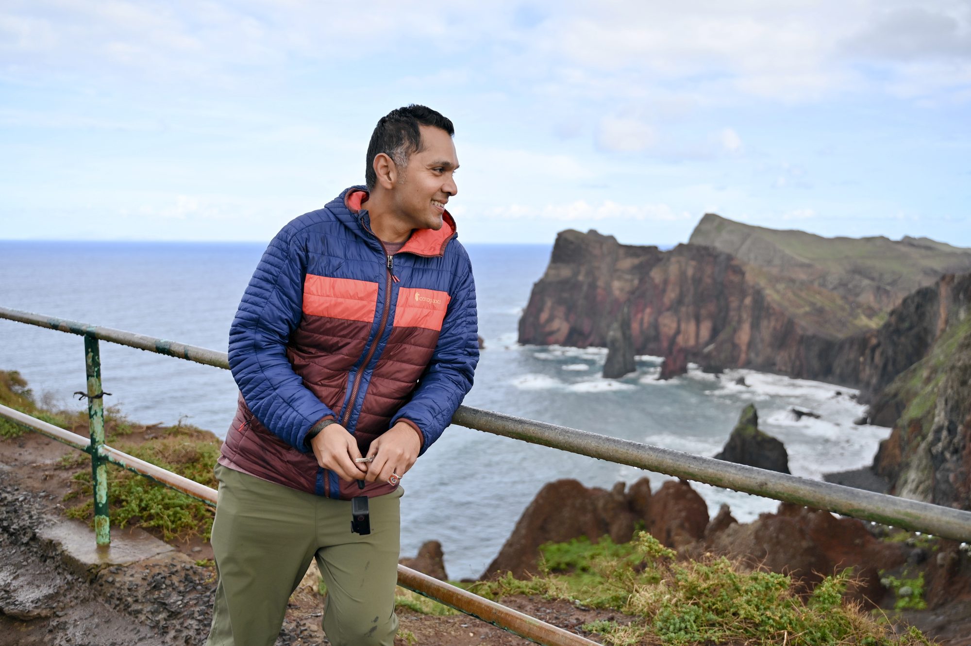 His dad leaning on the railing, with red cliffs and rocks in the sea behind him.