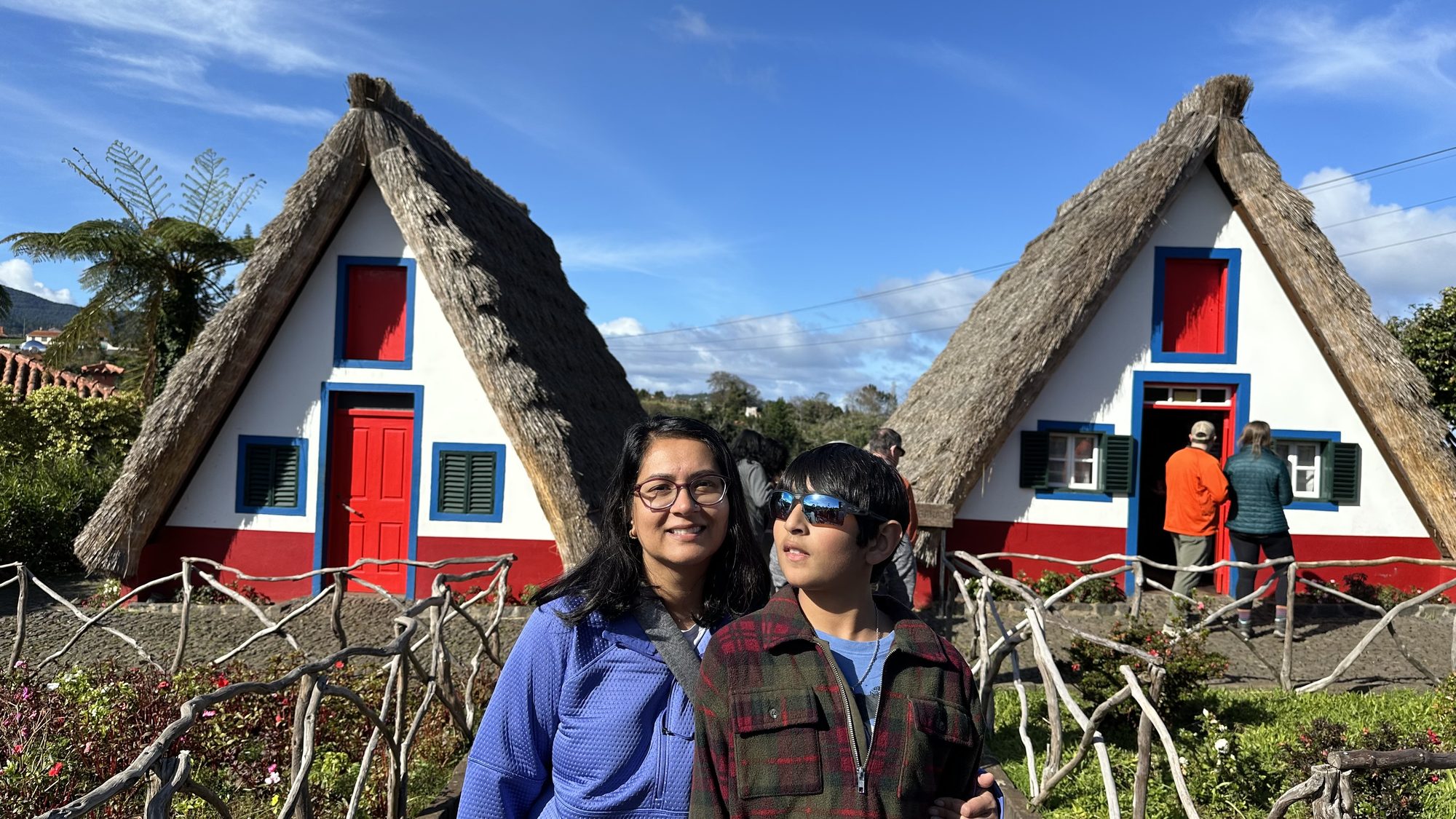 Two of us in front of two thatched Santana houses with red doors, under a blue sky.