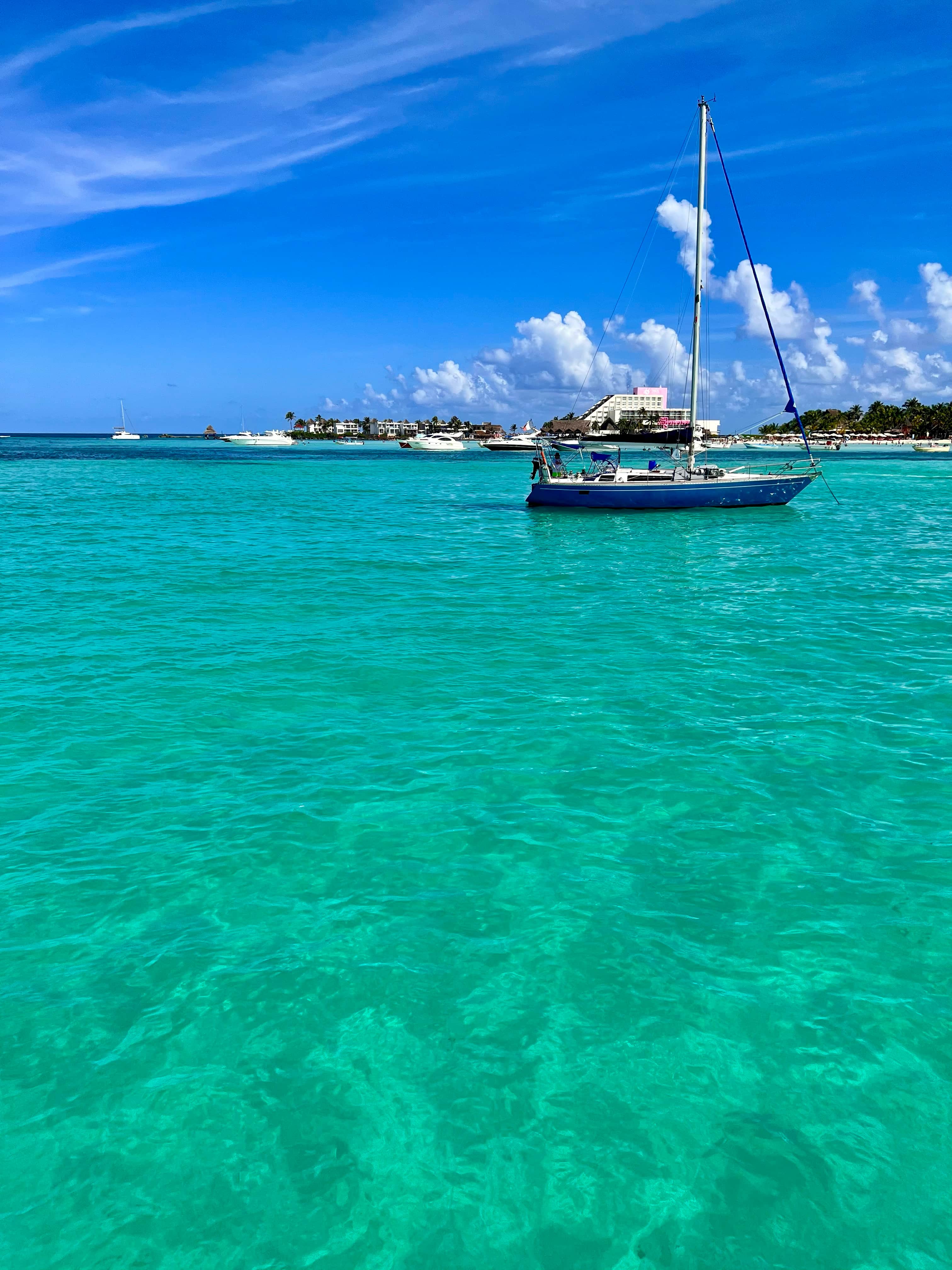 Boat with sail folded on a shallow sea with an island resort and other boats in the background