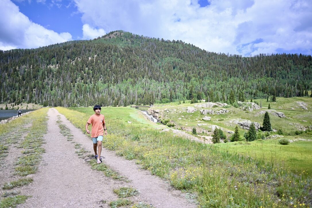 Boy walking a dirt road beside the Big Meadows Reservoir below forested hills
