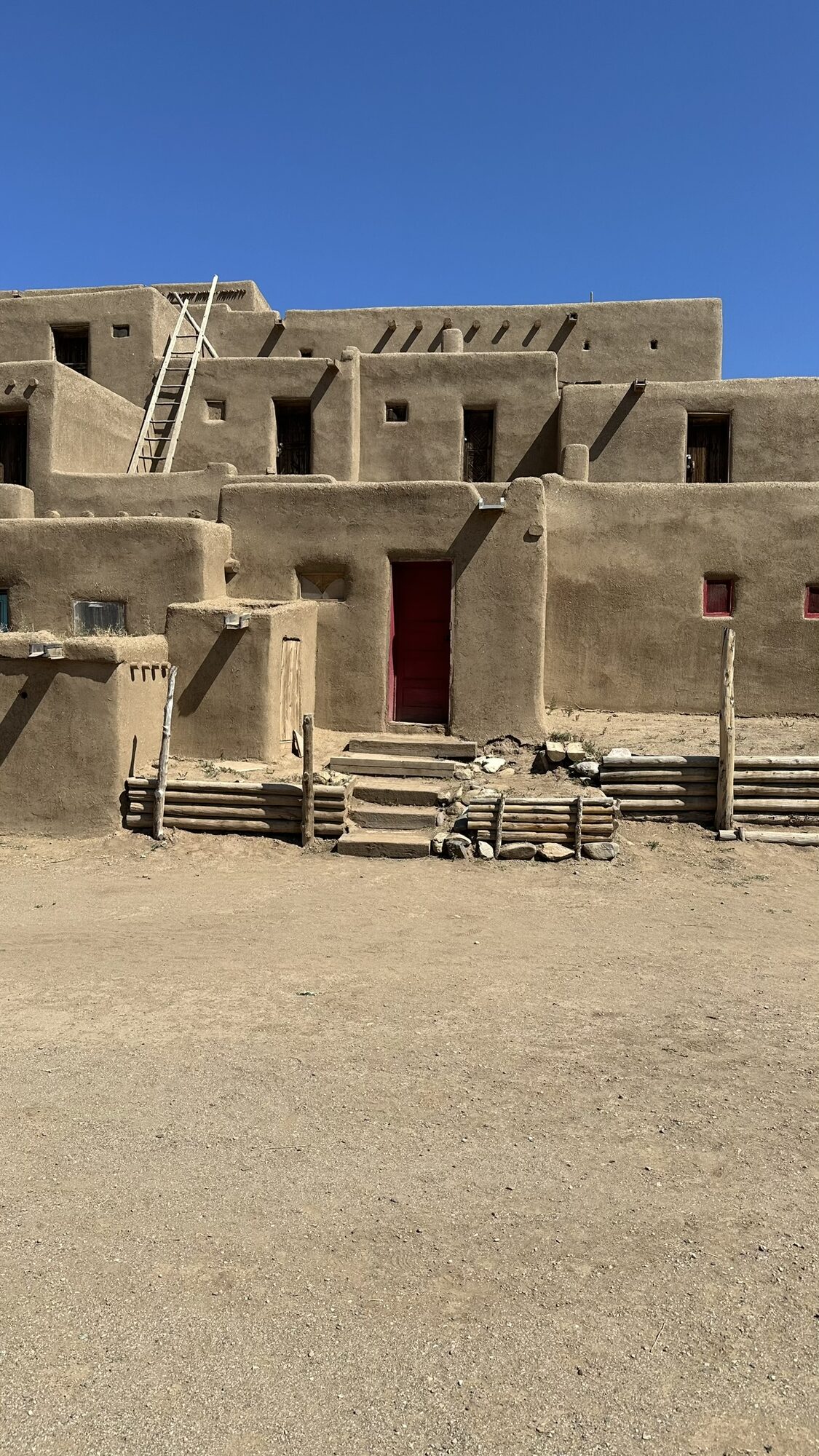Multi-story adobe dwellings at Taos Pueblo under a blue sky