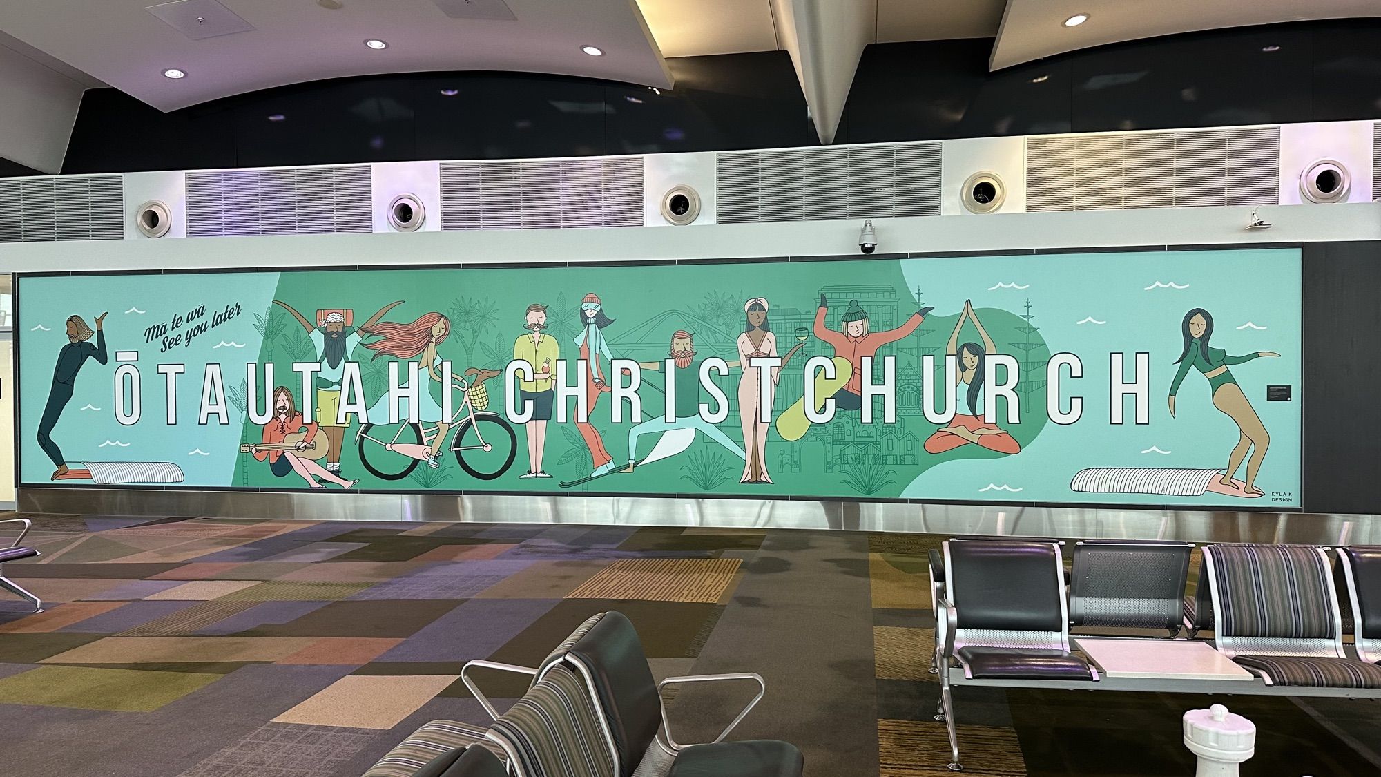 A long illustrated mural reading “Ōtautahi Christchurch” above rows of seats in the airport terminal.