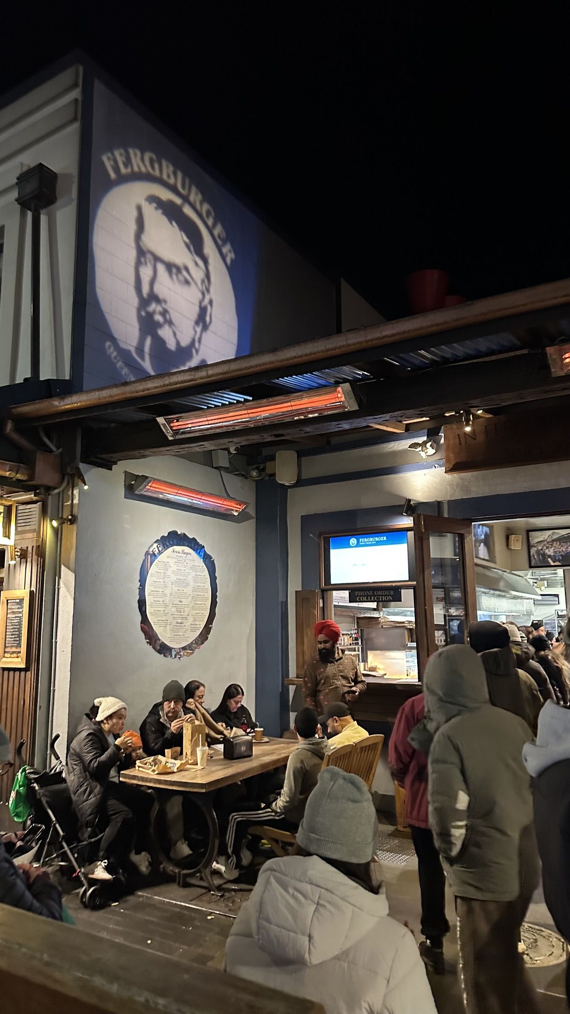 The busy front of Fergburger at night, with people eating at outdoor tables under heaters.