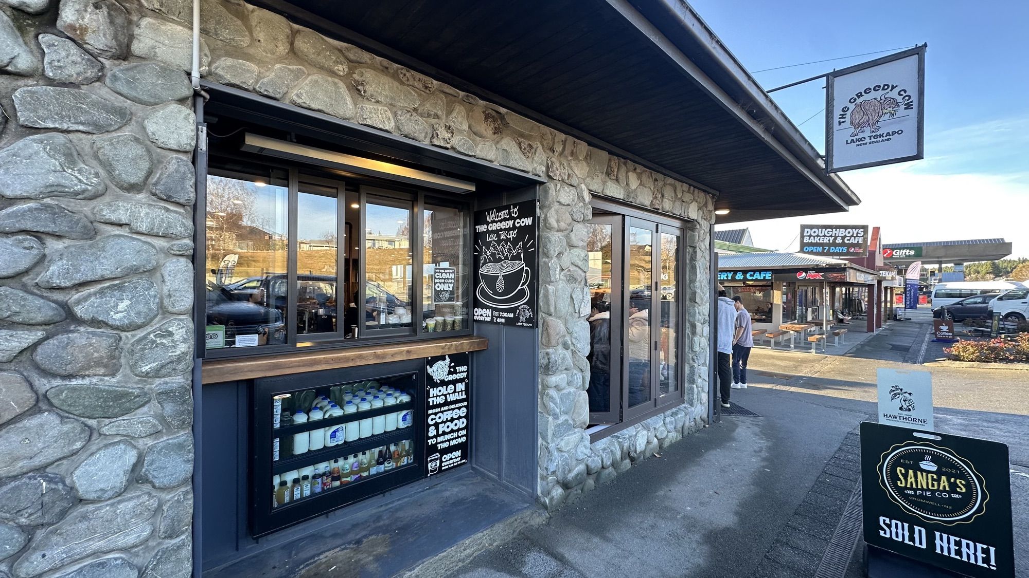 The stone front of the Greedy Cow café, with a small takeaway window and a sandwich board outside.