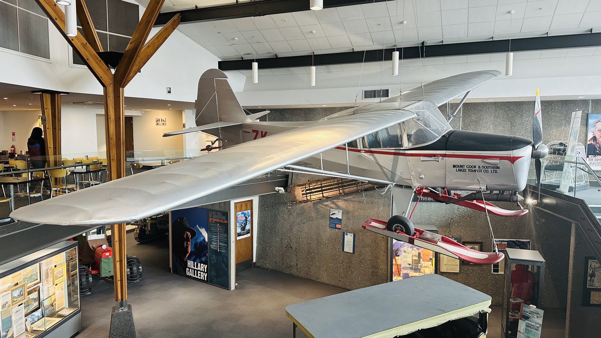 A vintage ski plane suspended from the ceiling of a museum hall, with displays below.