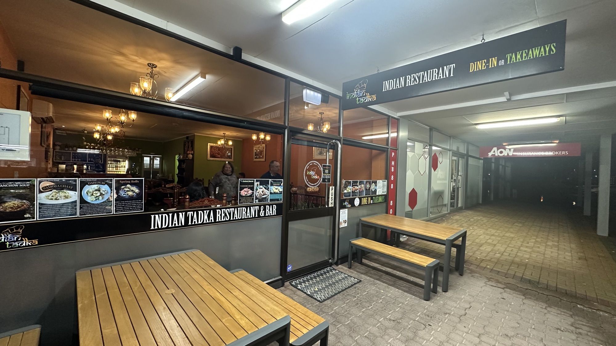 The front of Indian Tadka Restaurant & Bar in a covered arcade, with wooden picnic tables outside.