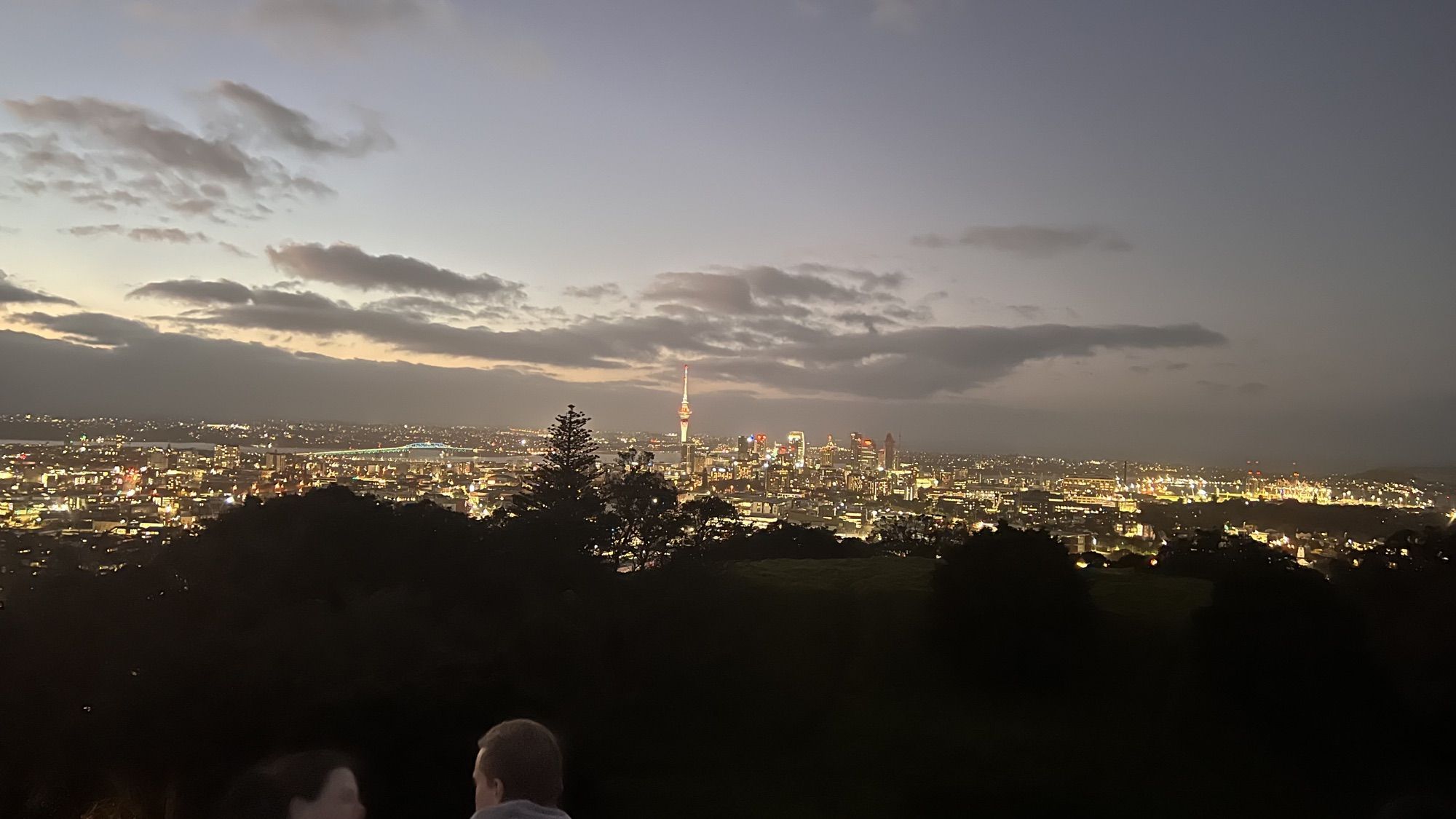 Auckland’s city lights and the illuminated Sky Tower spread out below a dusky sky, seen from the top of Mount Eden.