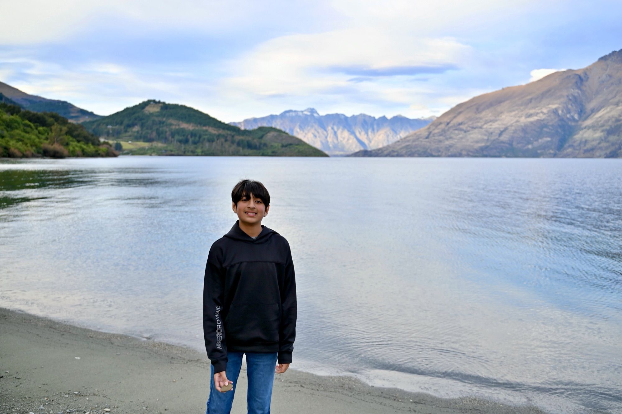 Our son standing on the lakeshore, with Lake Wakatipu and the mountains behind him.