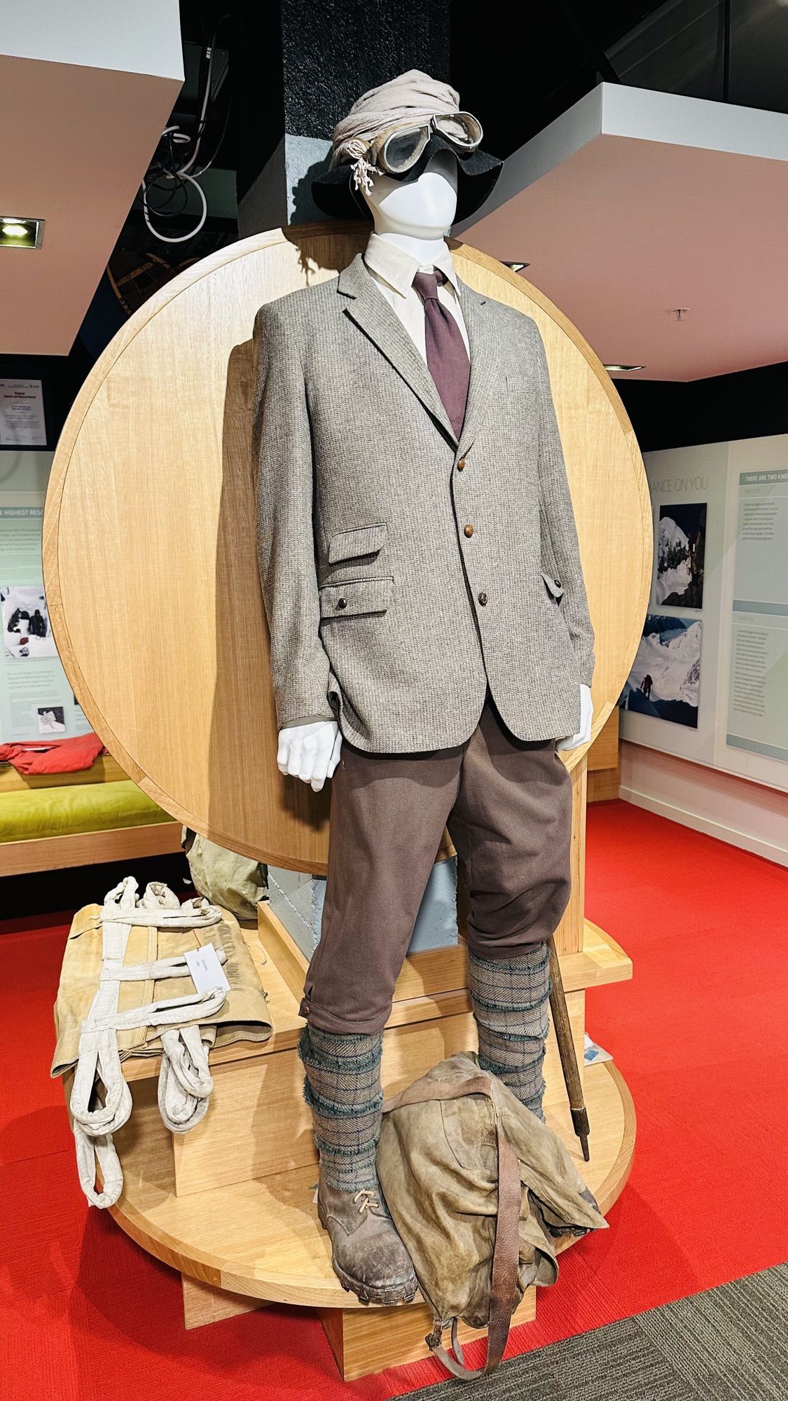 A mannequin in an old tweed climbing outfit with goggles, rope and a canvas pack in a museum display.