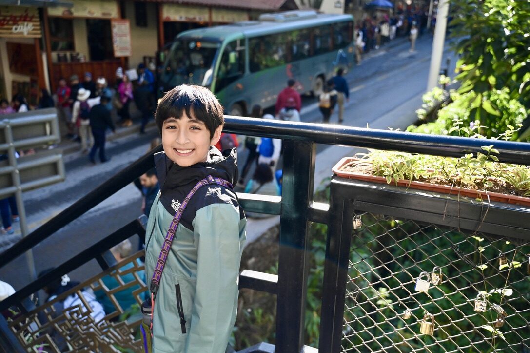 Boy smiling at a railing above the street where the Machu Picchu buses wait