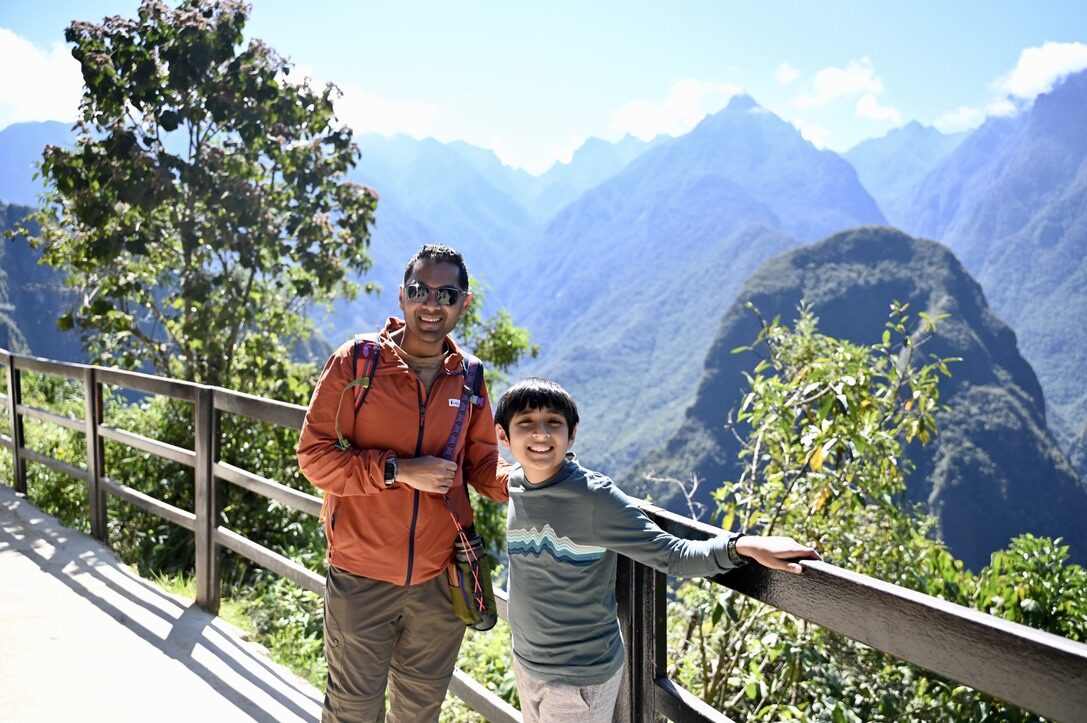 Man and boy at a wooden railing with green mountains behind