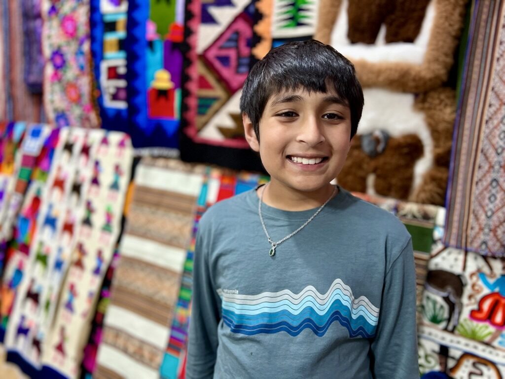 Boy smiling in front of stacks of colorful woven textiles