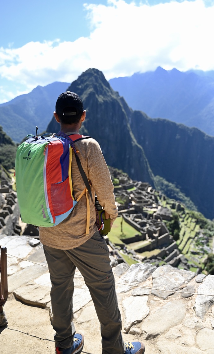 Man with backpack looking at mountains. The mid picture has a mountain top covered with the Incan ruins of Machu Picchu.