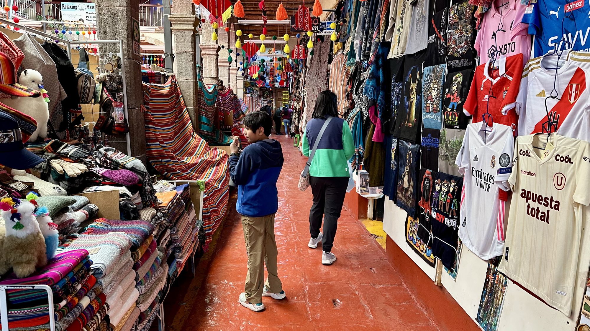 Woman and boy walking past stalls of colorful textiles and football shirts