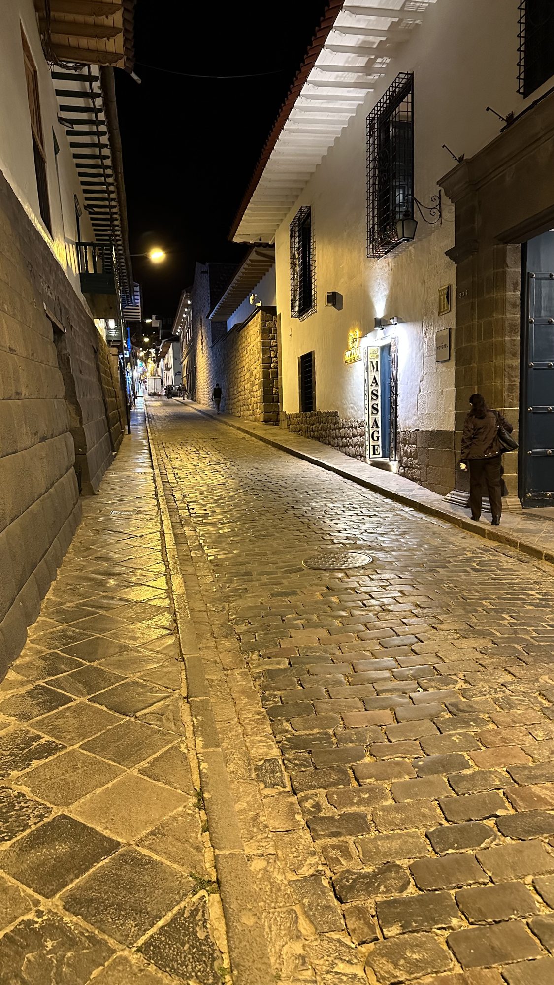 A quiet cobbled street in Cusco at night, lit by street lamps