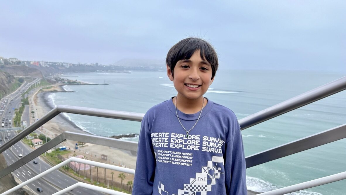 Boy smiling at a railing above the ocean and coastal highway at Larcomar
