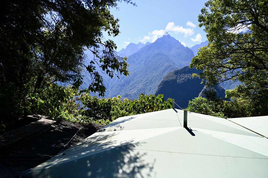 Lush mountain peaks in the background, with midground of tropical trees and foreground of canopied roof tops of commerical buildings