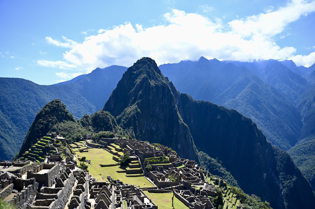 The image depicts a city nestled in the mountains, showcasing a picturesque landscape characterized by highlands and ridges. The sky is adorned with clouds, adding to the serene ambiance of the valley below. This scenic location is ideal for travel enthusiasts looking to explore nature's beauty amid mountain ranges and grassy hills.