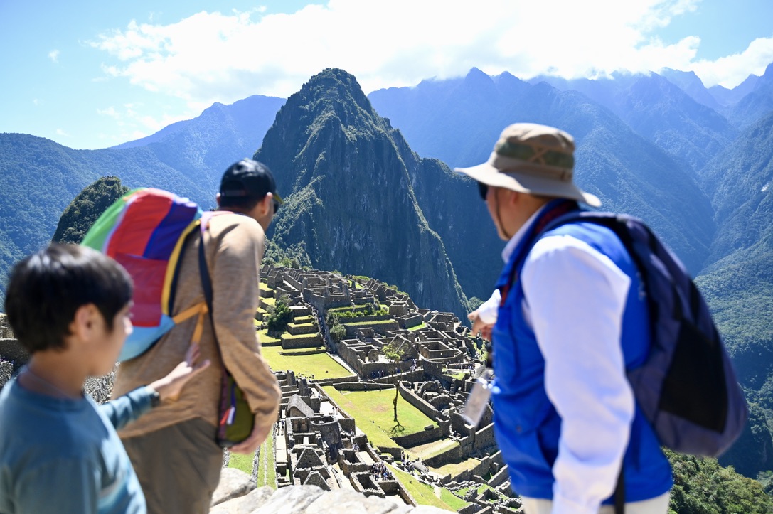 A group of people is gathered outdoors looking at a vista. They are dressed in hiking clothing and appear to be planning their next move in a mountainous area. The sky suggests they are enjoying a clear day suitable for travel and exploration.