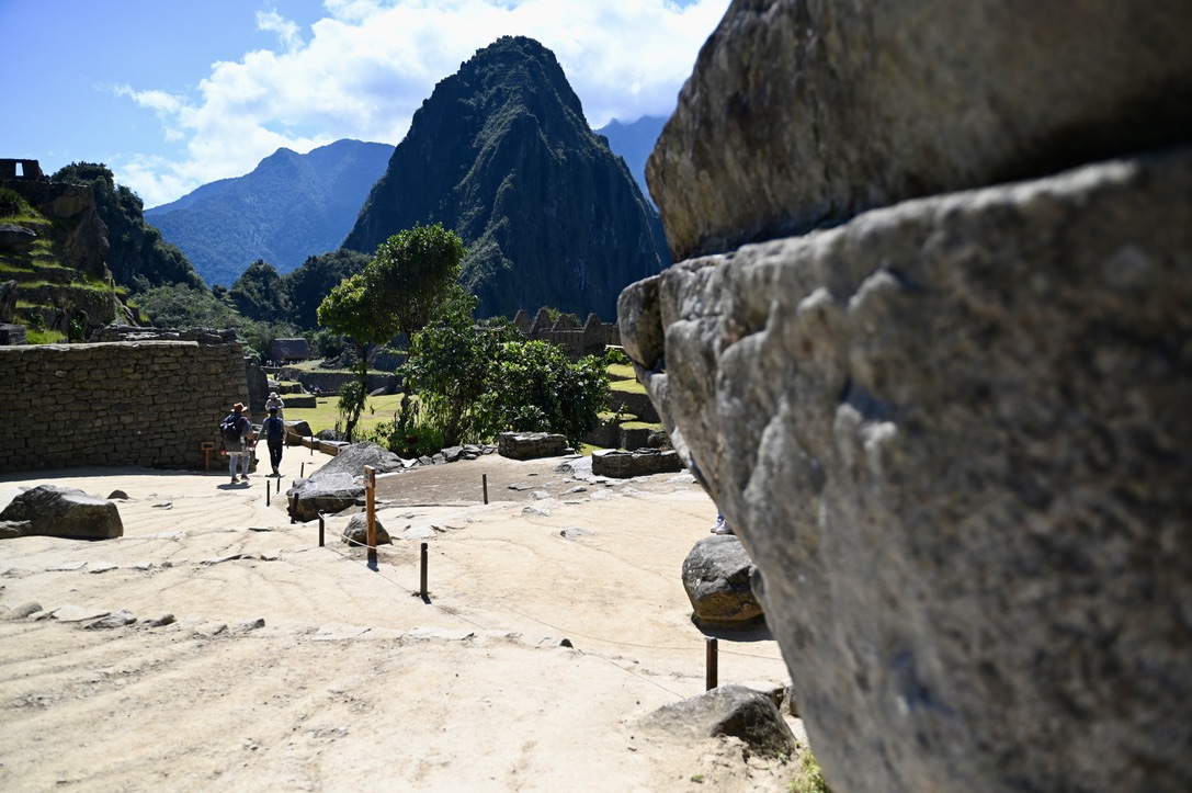 View of Machu Picchu from a stone wall looking at stone pathways, grassy fields and tropical jungle covered mountain peaks in the background