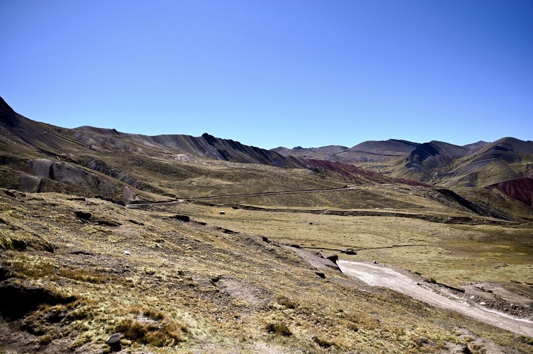 A trail curving across a dry valley with faint red and purple streaks on the hills