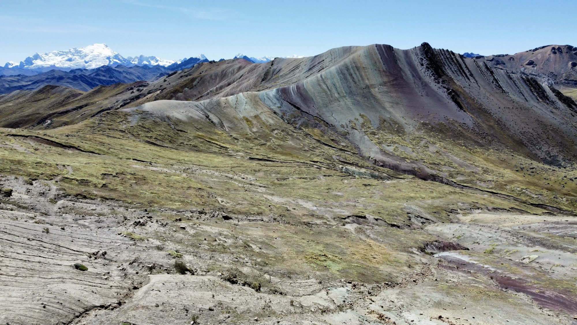 Striped rainbow mountains with snow-covered peaks on the horizon