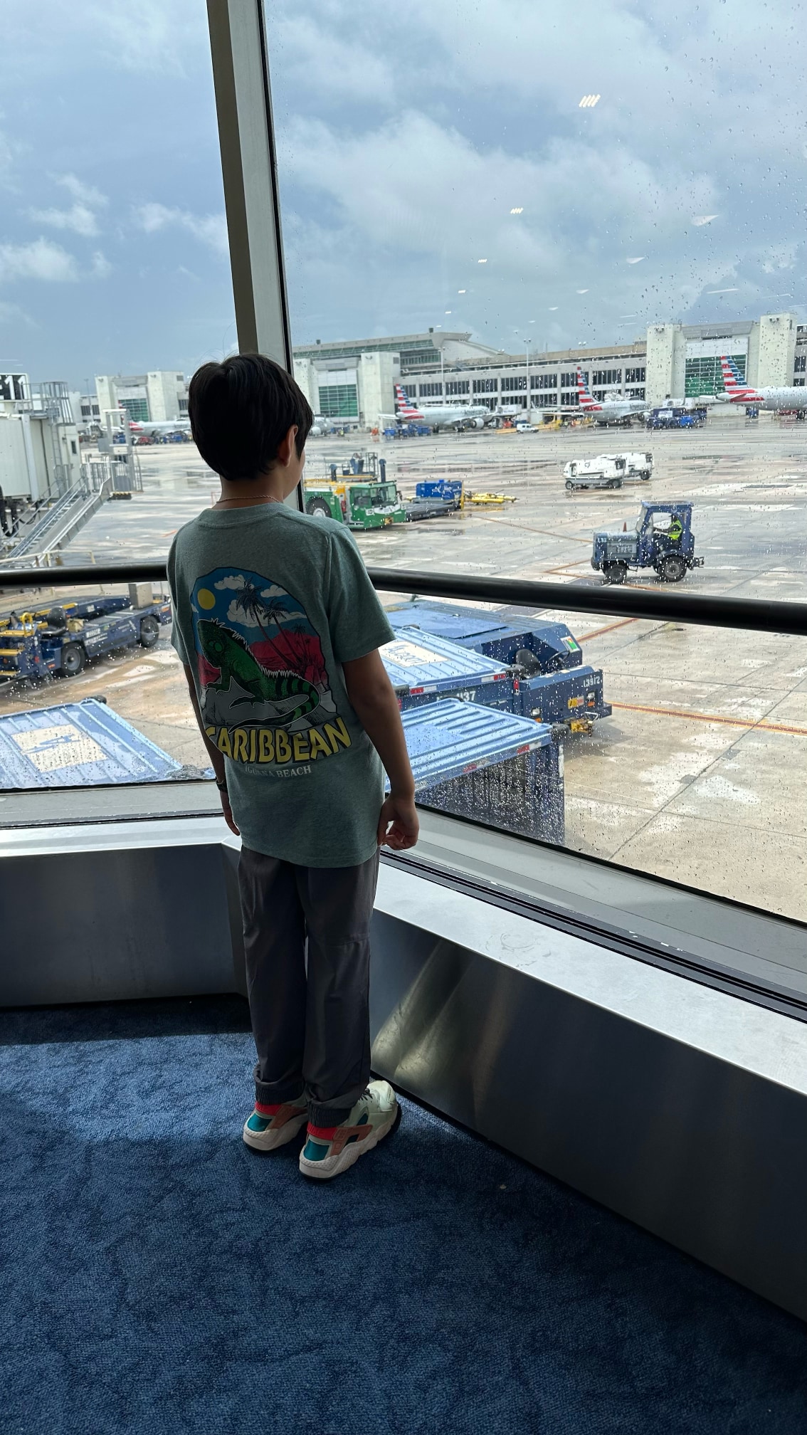 Boy watching the ground operations at an airport terminal in Miami international, through glass window with rain drops