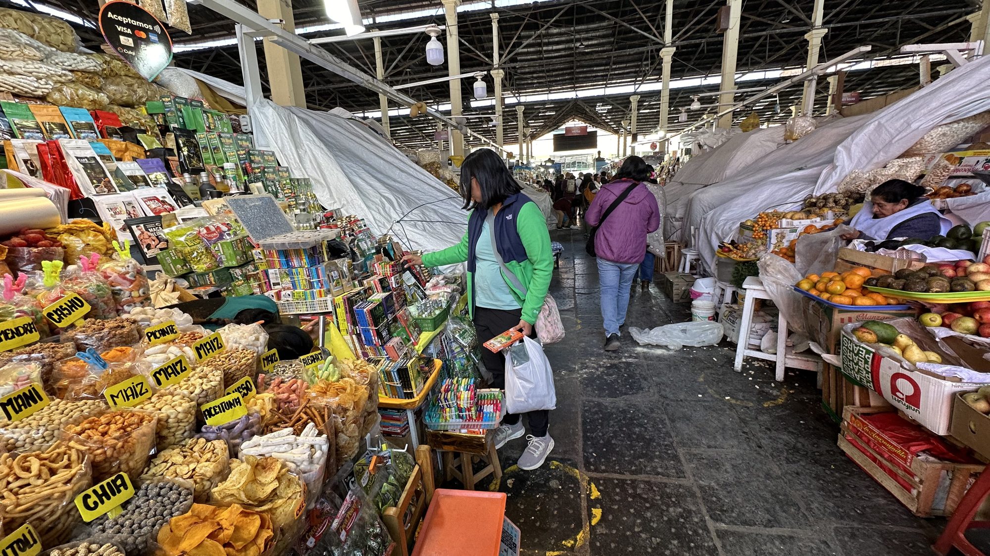 A woman browsing stalls piled with fruit and snacks inside San Pedro Market