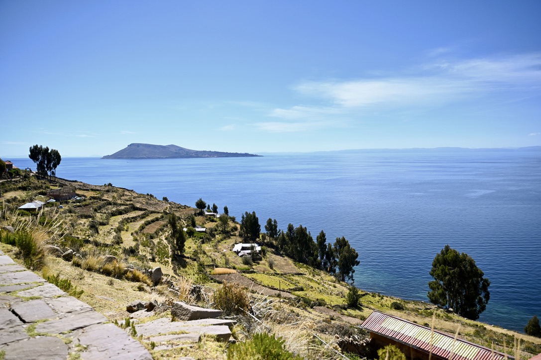 Viewpoint from side of a hill with vast open water lake with an island in the distance. The hill side is covered by terraced fields