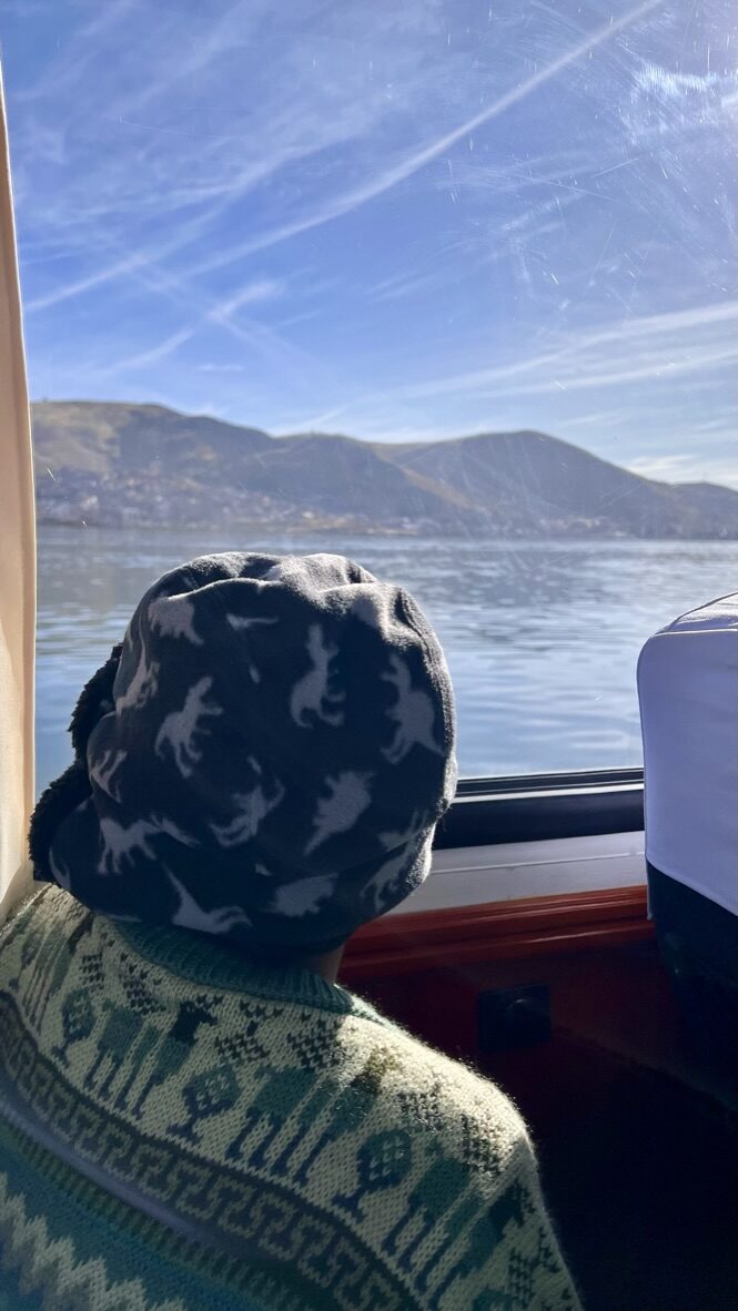 Boy looking out the boat window at the lake and hills