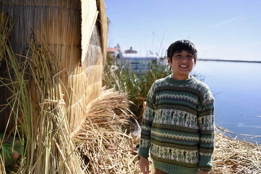Boy smiling beside a reed hut on the island, with the lake behind