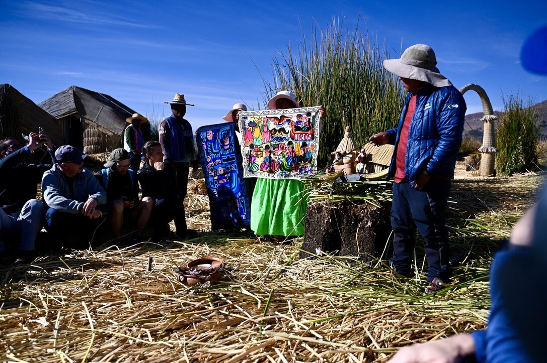 A family on a reed island explaining their way of life to visitors seated on reed benches