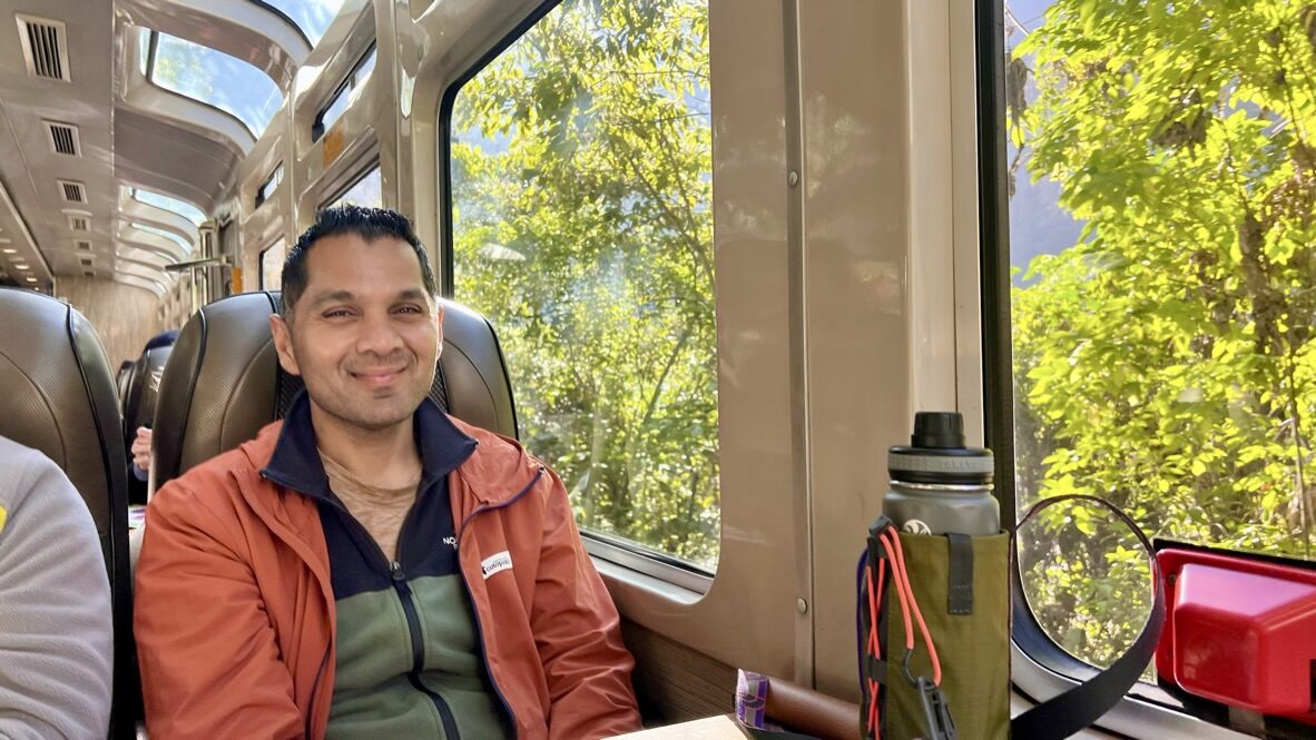 Man smiling in a Vistadome seat with large windows onto the green valley