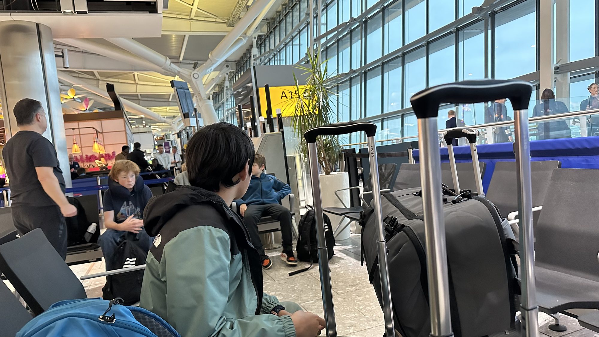Our family waiting at the departure gate with carry-on bags, in a bright terminal with tall glass windows.