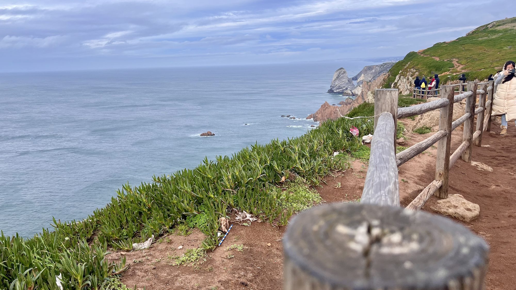 A fenced dirt path along a green clifftop high above the Atlantic at Cabo da Roca.