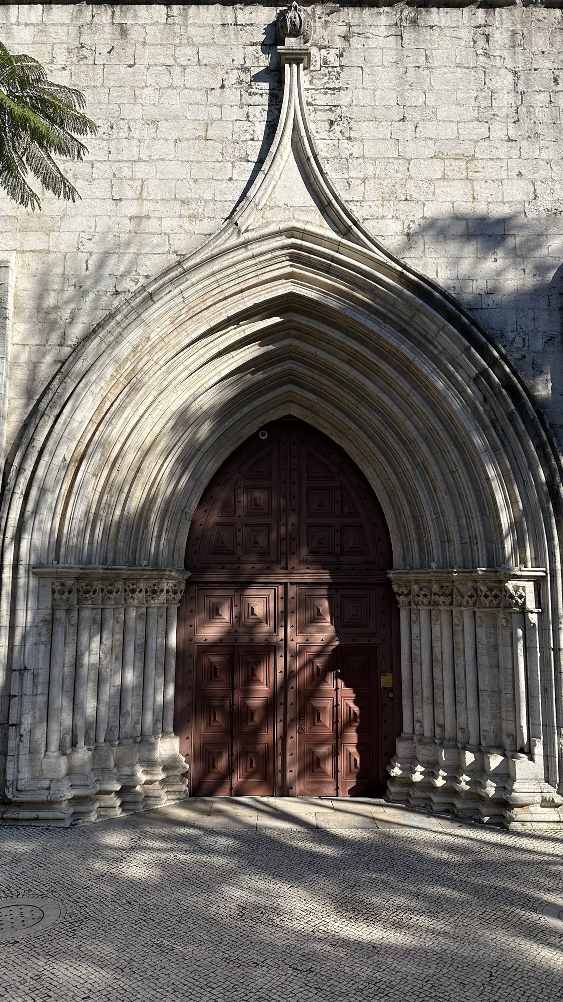 The pointed Gothic stone archway and dark red wooden door of the Carmo Convent.