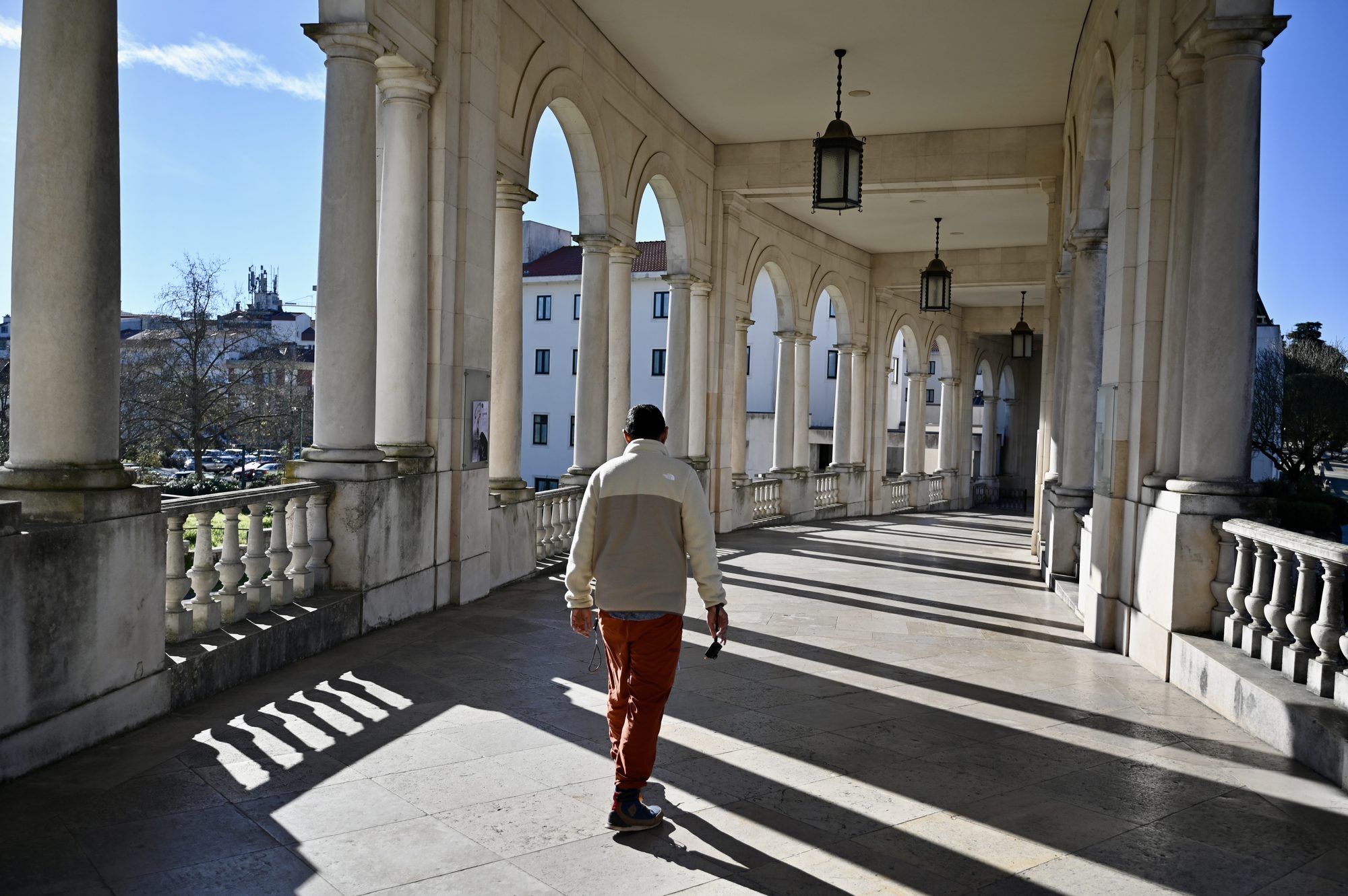 One of us walking along a sunlit colonnade of white columns and arches at the sanctuary.