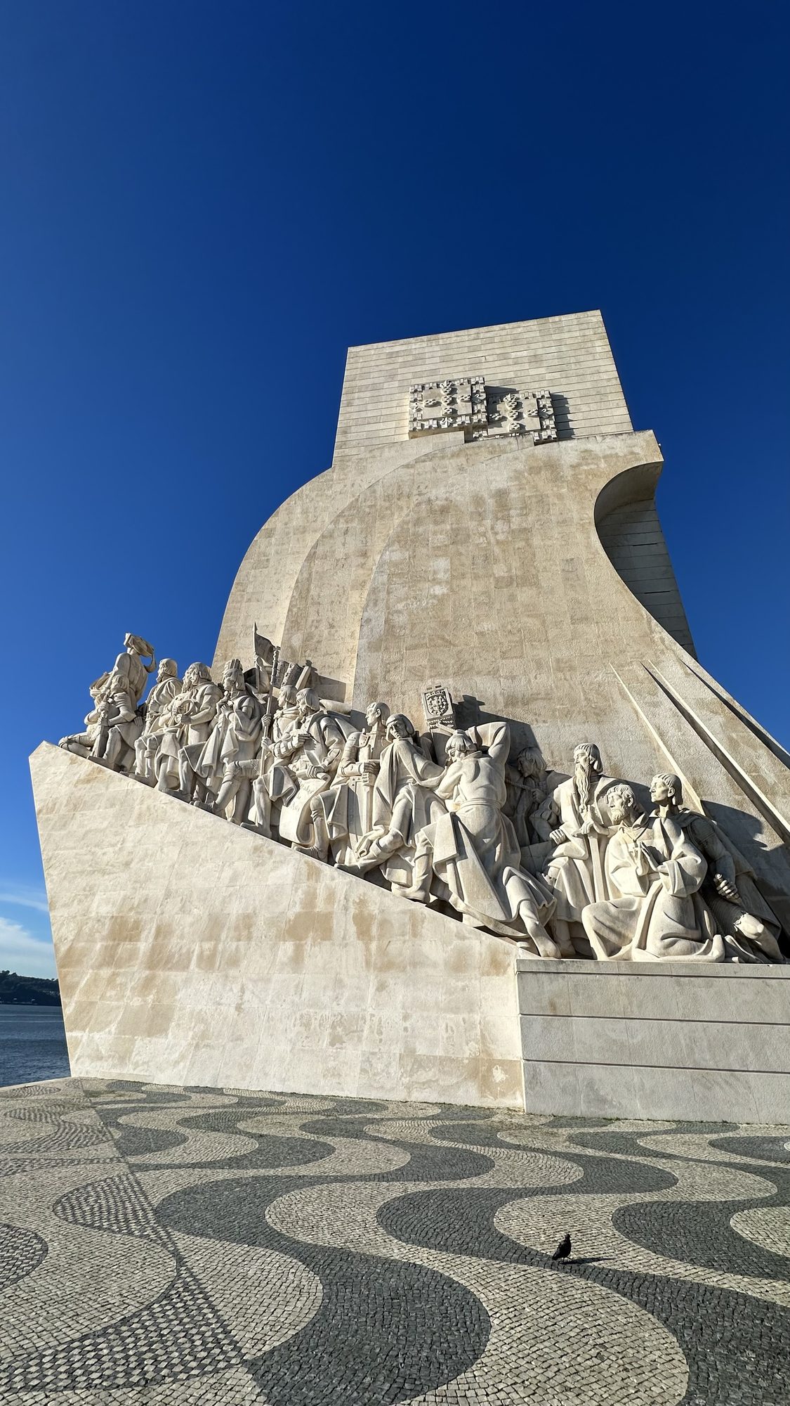 The Monument to the Discoveries, a tall white stone prow lined with carved explorers, rising above a wave-patterned mosaic pavement.