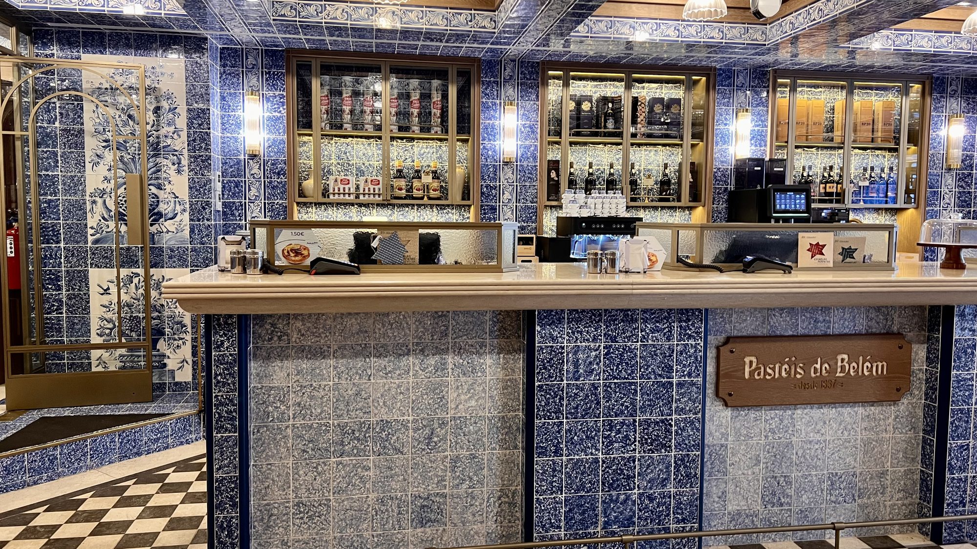 The counter at Pastéis de Belém, with blue-and-white tiled walls and a wooden sign bearing the bakery’s name.