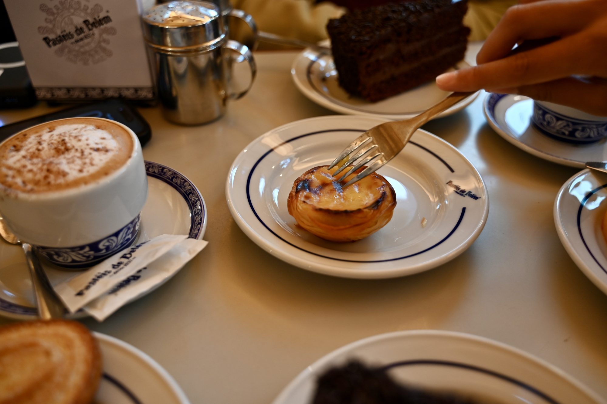 A pastel de nata on a blue-rimmed plate next to a cappuccino dusted with cinnamon.