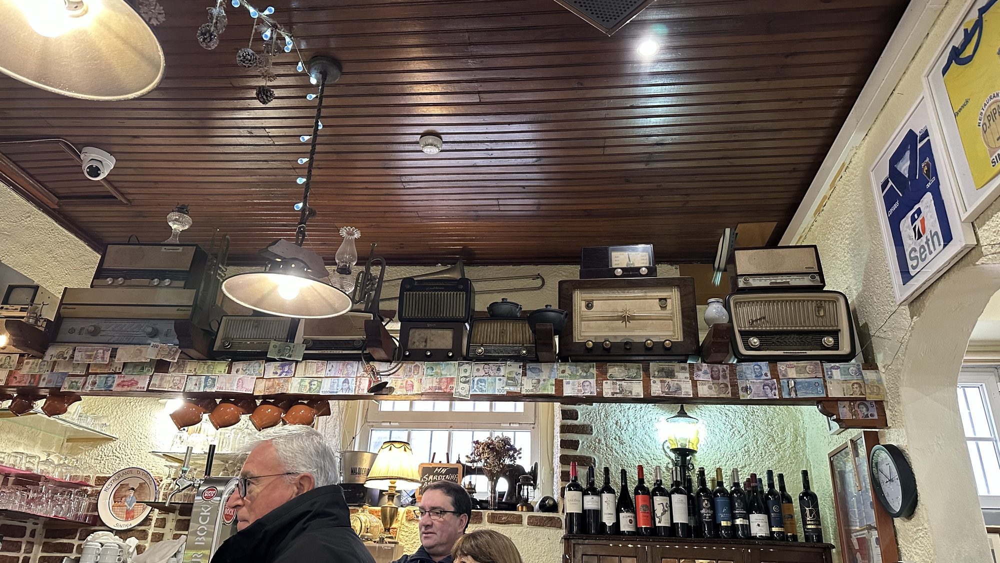 A cozy restaurant interior with vintage radios lining a shelf above the bar and rows of wine bottles.
